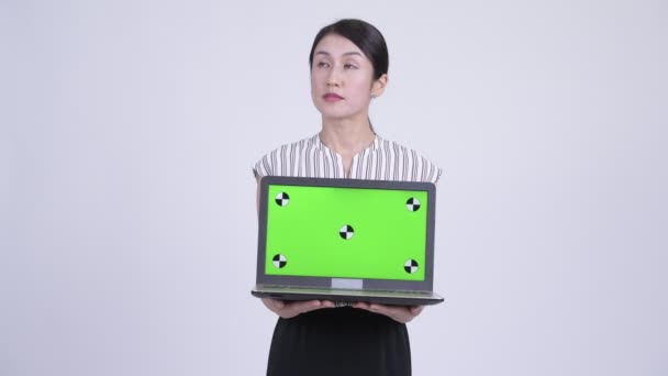 Happy beautiful Asian businesswoman thinking while showing laptop — Stock Video