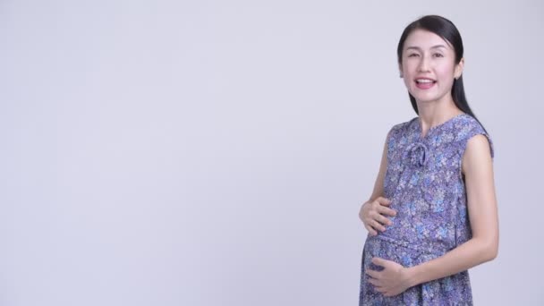 Glad gravid asiatisk kvinna visar något på baksidan — Stockvideo