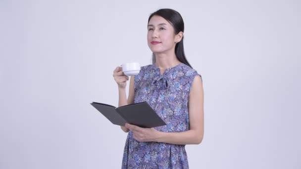 Счастливая беременная азиатка читает книги и пьет кофе — стоковое видео