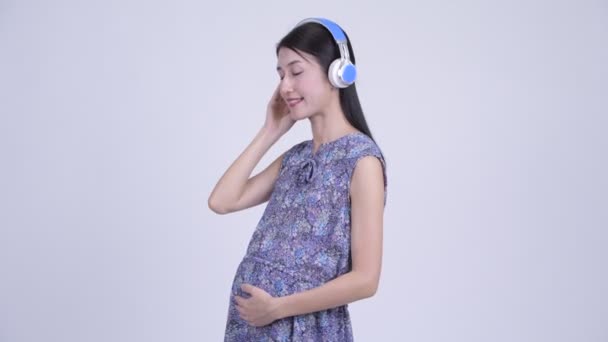 Счастливая беременная азиатка слушает музыку — стоковое видео