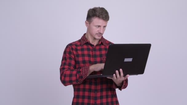 Feliz barbudo hipster hombre pensando mientras se utiliza el ordenador portátil — Vídeo de stock