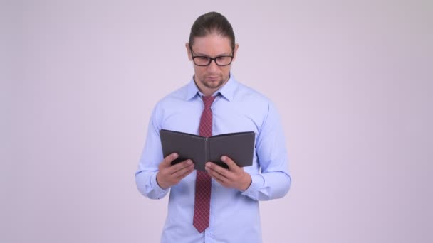 Verlegen knappe zakenman die betrekking hebben op gezicht met boek — Stockvideo