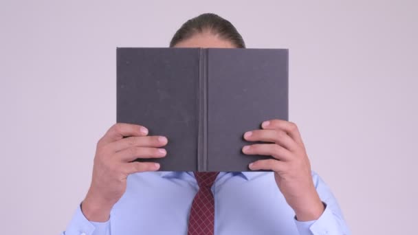Gesicht des schüchternen Geschäftsmannes, der denkt, während er sein Gesicht mit einem Buch verhüllt — Stockvideo