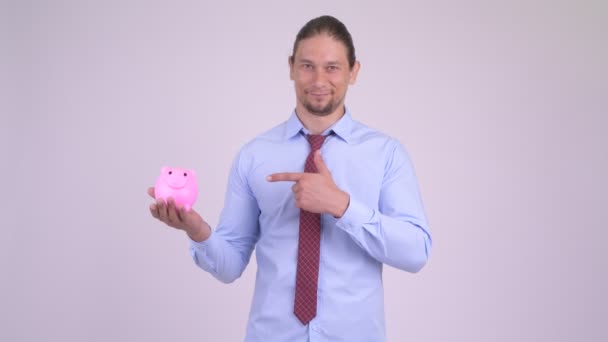Счастливый красивый бизнесмен держит копилку и показывает большие пальцы — стоковое видео