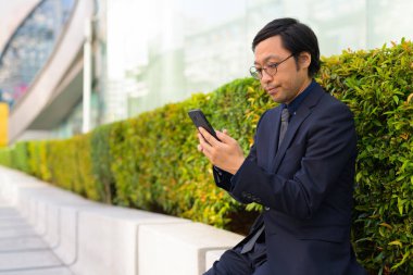 Telefon açık havada kullanırken oturan Asya iş adamı