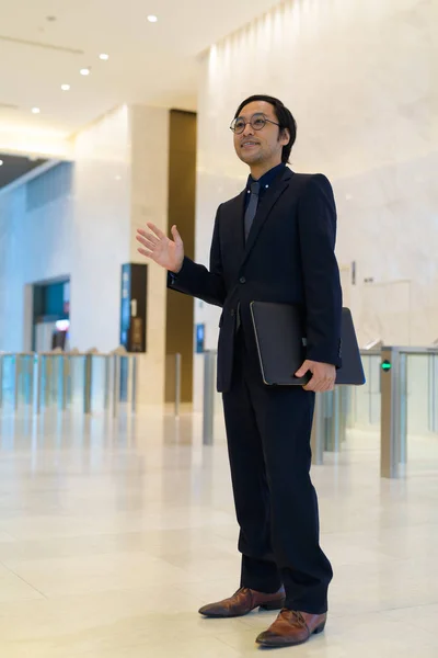 Plan complet du corps de heureux homme d'affaires asiatique tenant un ordinateur portable et agitant la main — Photo