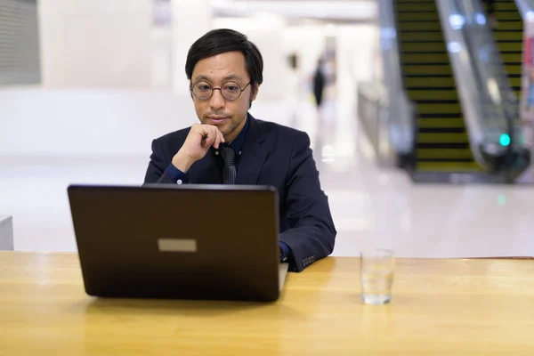 Ázsiai üzletember gondolkodás közben használ laptop belül az irodaház — Stock Fotó
