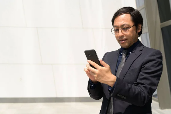 Asiático hombre de negocios usando teléfono contra concreto pared al aire libre —  Fotos de Stock