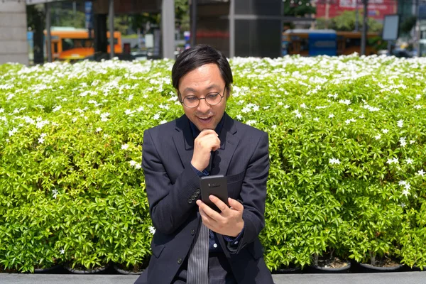 Heureux homme d'affaires asiatique penser tout en utilisant le téléphone avec la nature dans la ville — Photo
