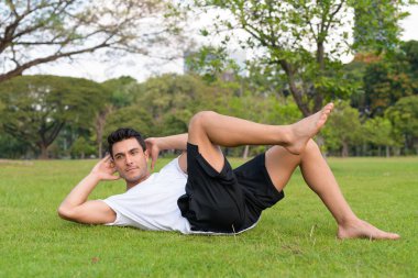 Genç yakışıklı İspanyol adam parkta oturup yapıyor