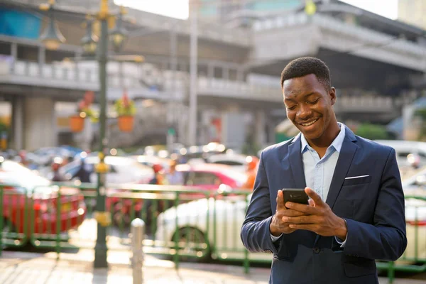 Jovem empresário africano feliz usando telefone na cidade — Fotografia de Stock