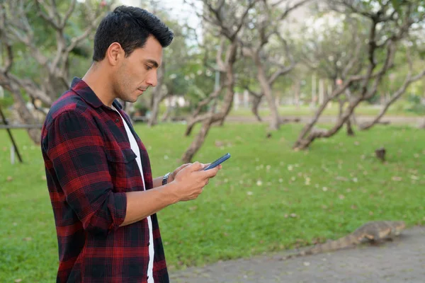 Vue du profil d'un jeune hipster hispanique qui utilise son téléphone au parc — Photo