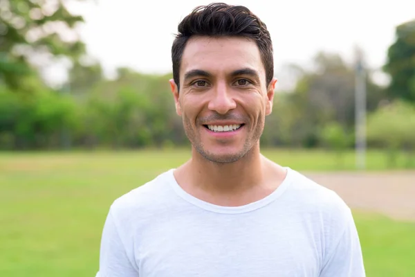 Face of happy young handsome Hispanic man smiling at the park — Stock Photo, Image