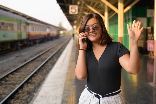 Šťastné mladé asijské turistické žena mluví po telefonu a mávání rukou na nádraží — Stock fotografie