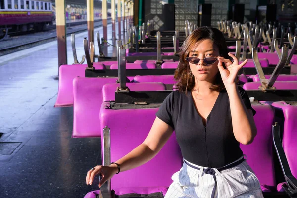 Jeune belle femme touristique asiatique tenant des lunettes de soleil et assis sur une chaise rose — Photo