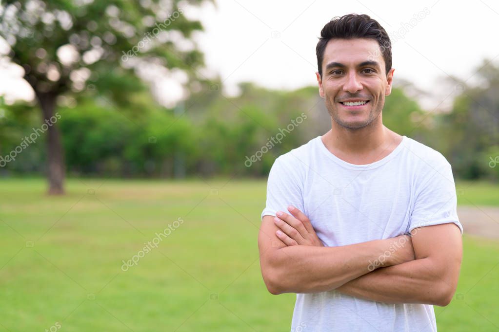 Happy young Hispanic man smiling with arms crossed in the park outdoors