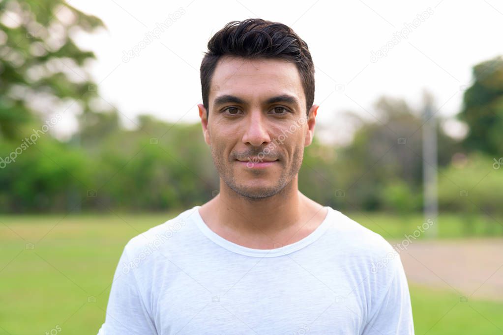 Face of young handsome Hispanic man at the park
