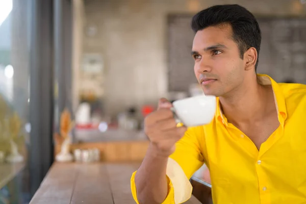 Jeune homme indien beau boire du café tout en regardant par la fenêtre au café — Photo