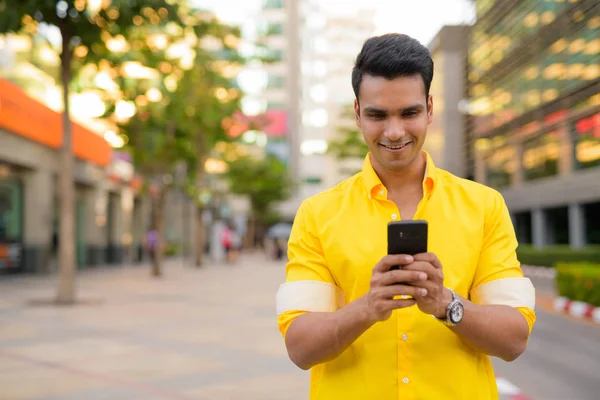 Happy young handsome Indian man using phone in the city street — Stock Photo, Image