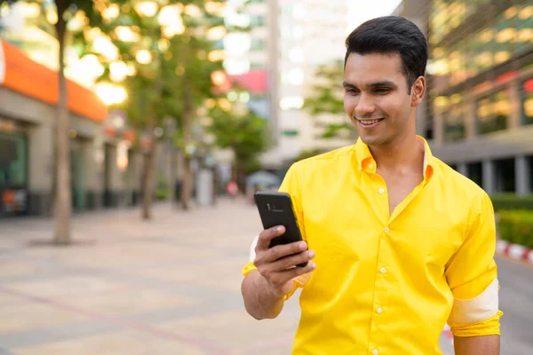 Happy young handsome Indian man using phone in the city street — Stock Photo, Image