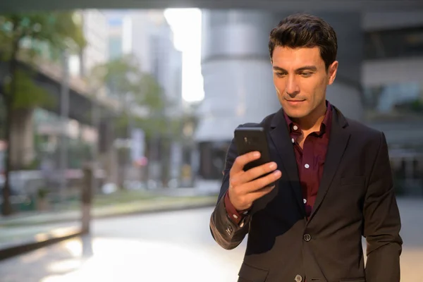 Jeune homme d'affaires hispanique beau utilisant le téléphone à l'extérieur de l'immeuble de bureaux — Photo