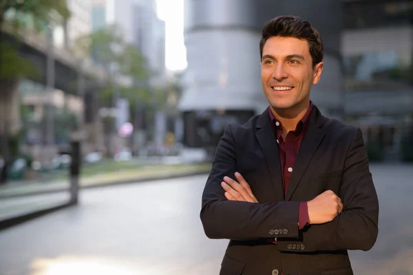 Joven empresario hispano feliz pensando con los brazos cruzados fuera del edificio de oficinas — Foto de Stock