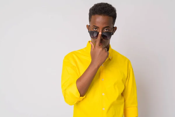 Молодой африканский бизнесмен в жёлтой рубашке подглядывает в солнечные очки — стоковое фото