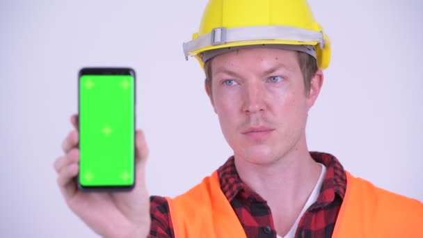 Visage de jeune homme heureux travailleur de la construction montrant téléphone — Video