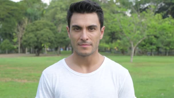 Gesicht eines fröhlichen jungen, gut aussehenden hispanischen Mannes, der im Park lächelt — Stockvideo