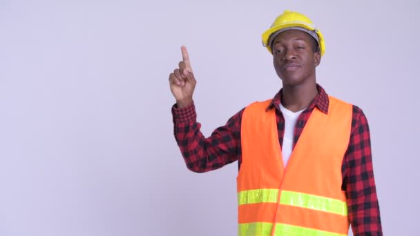 Joven feliz africano trabajador de la construcción pensando mientras señala hacia arriba — Vídeos de Stock