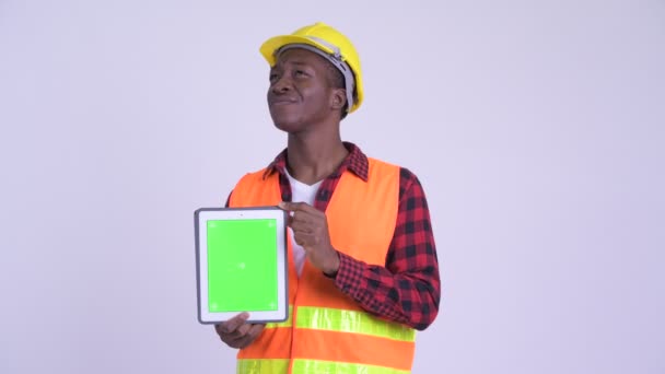 Молодой счастливый африканский рабочий строитель думает, показывая цифровой планшет — стоковое видео