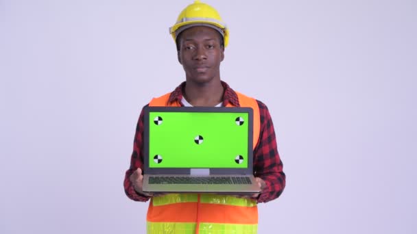 Joven hombre africano feliz trabajador de la construcción mostrando el ordenador portátil y mirando sorprendido — Vídeos de Stock