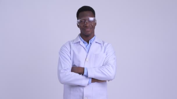 Молодой счастливый африканский врач в защитных очках, улыбающийся со скрещенными руками — стоковое видео