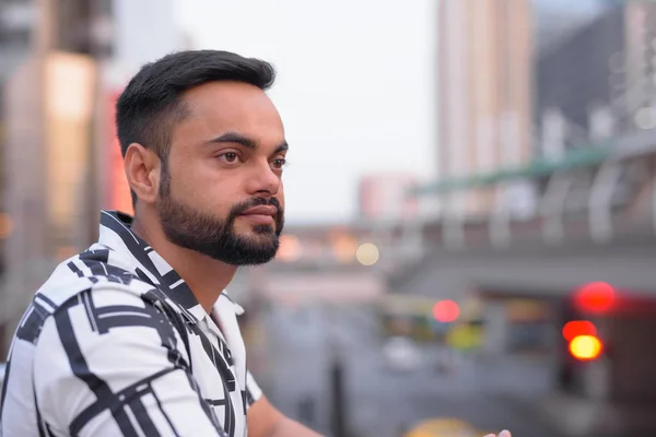 Gesicht eines jungen bärtigen indischen Mannes, der gegen den Blick auf die Stadt im Freien denkt — Stockfoto