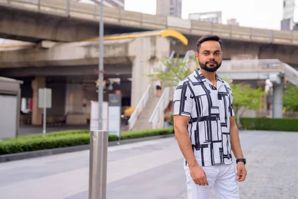 Young bearded Indian man against view of the skytrain station outdoors