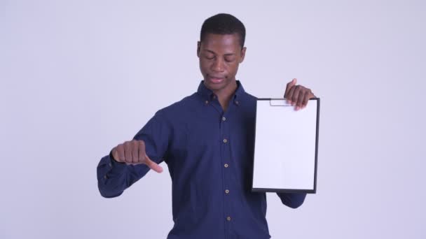 Jonge beklemtoonde Afrikaanse zakenman die duimen neer geeft terwijl het tonen van Klembord — Stockvideo
