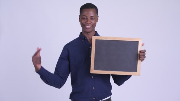 Young happy African businessman holding blackboard and giving thumbs up — Stock Video