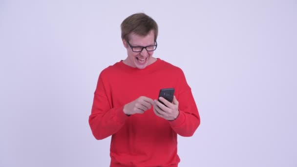 Jovem homem bonito feliz usando telefone e recebendo boas notícias — Vídeo de Stock