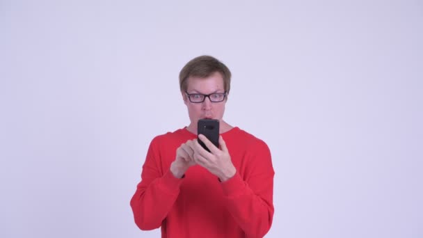 Лицо молодого человека, использующего телефон и выглядящего шокированным — стоковое видео