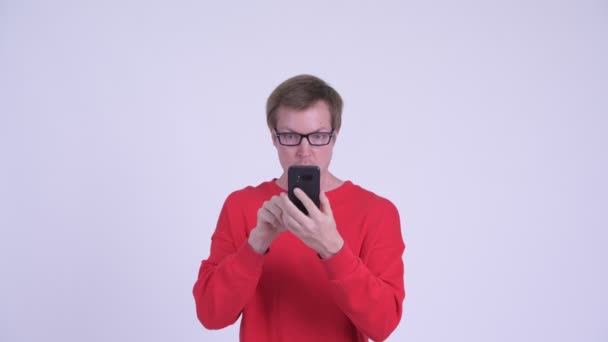 Πρόσωπο του νεαρού άντρα που χρησιμοποιεί το τηλέφωνο και φαίνεται σοκαρισμένος — Αρχείο Βίντεο