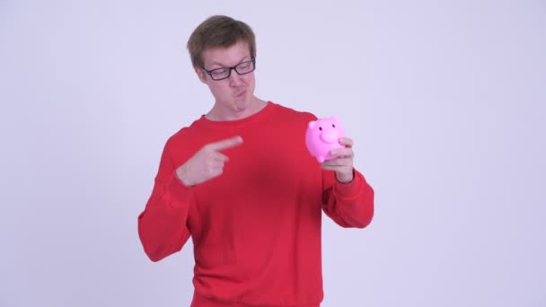 Mutlu genç yakışıklı adam tutan Piggy banka ve veren thumbs yukarı — Stok video