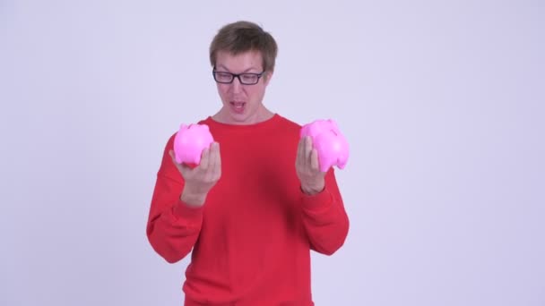 Happy young man playing with two piggy banks — Stock Video