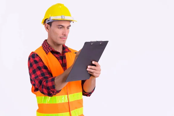 Joven y apuesto trabajador de la construcción hispano escribiendo en portapapeles —  Fotos de Stock