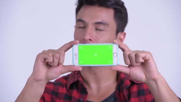 Gesicht eines glücklichen jungen hispanischen Hipster-Mannes, der beim Vorzeigen seines Telefons denkt — Stockvideo