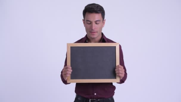 Młody szczęśliwy Hispanic biznesmen trzymający tablica i patrząc zaskoczony — Wideo stockowe