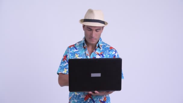 Young happy Hispanic tourist man thinking while using laptop — Stock Video