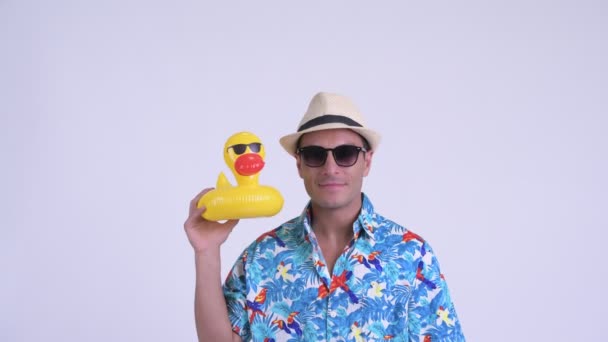 Gesicht eines jungen, fröhlichen hispanischen Touristenmannes mit Sonnenbrille, der eine aufblasbare Ente hält — Stockvideo