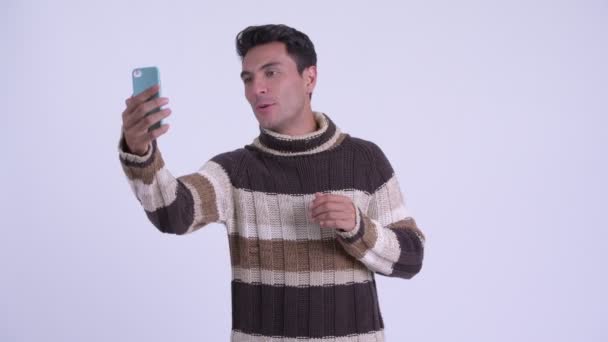 Joven feliz hombre hispano video llamadas y mostrando el teléfono listo para el invierno — Vídeo de stock