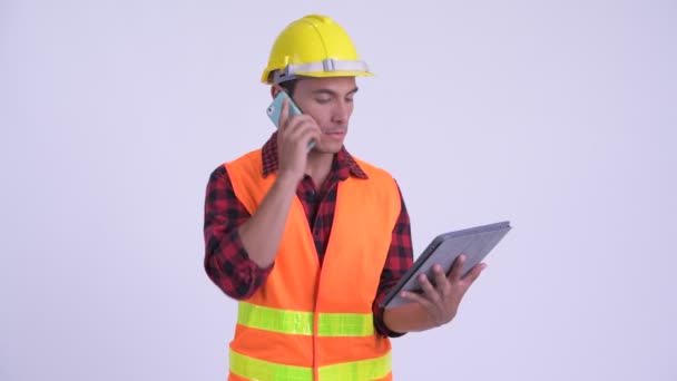 Νέος ευτυχισμένος ισπανόφωνων εργαζόμενος οικοδόμος χρησιμοποιώντας το τηλέφωνο και ψηφιακό δισκίο — Αρχείο Βίντεο