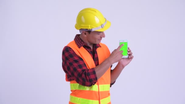 Joven feliz hispano trabajador de la construcción mostrando el teléfono y dando pulgares hacia arriba — Vídeos de Stock